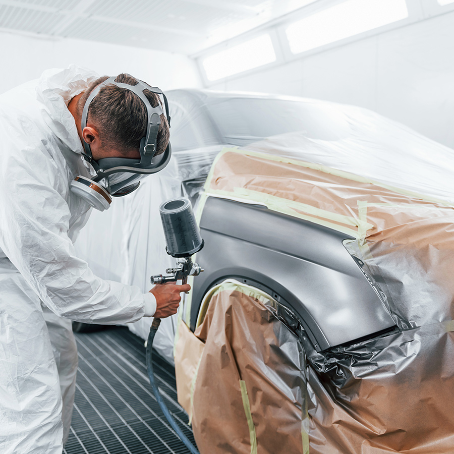 Automotive painter refinishing a car in a paint booth